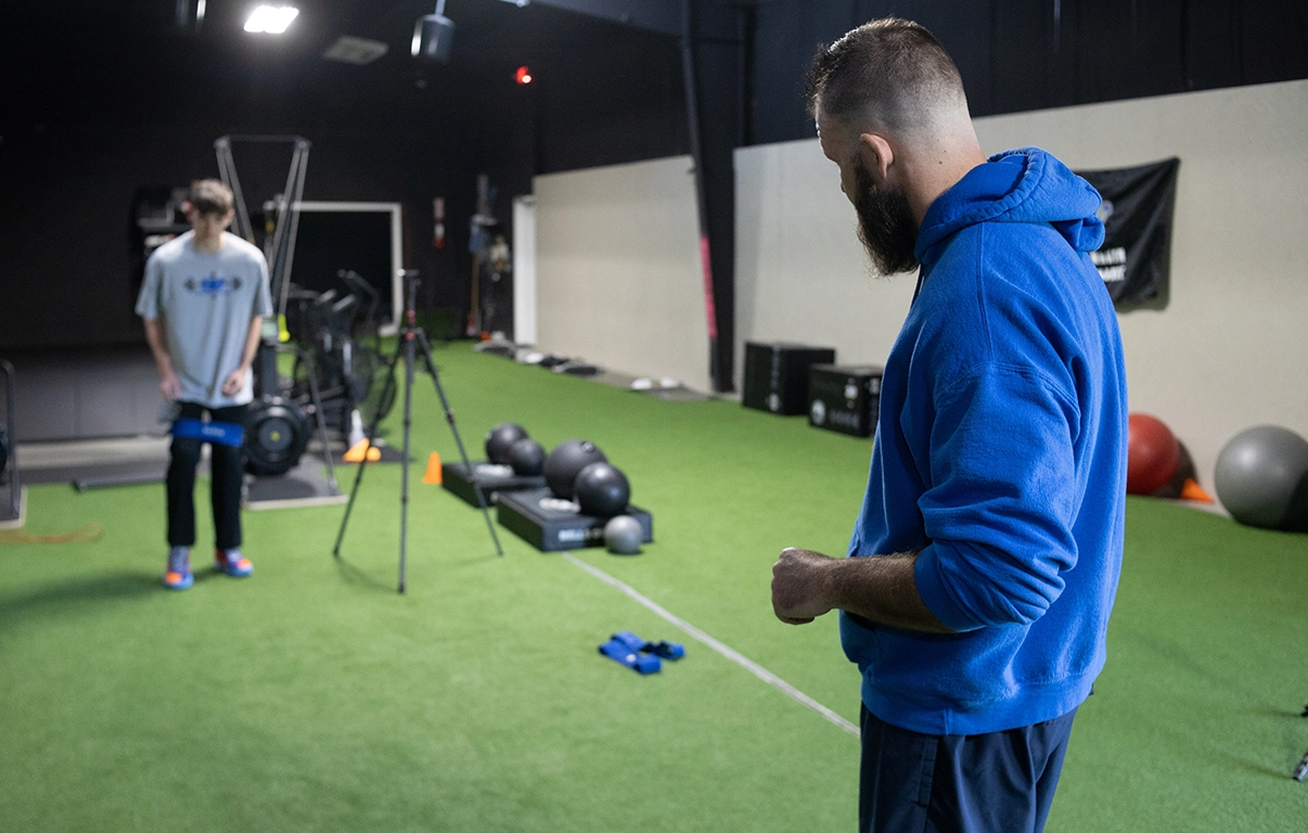 Collegiate athlete in a resistance band warm-up under Alex Makin's supervision during a collegiate athletic training session.